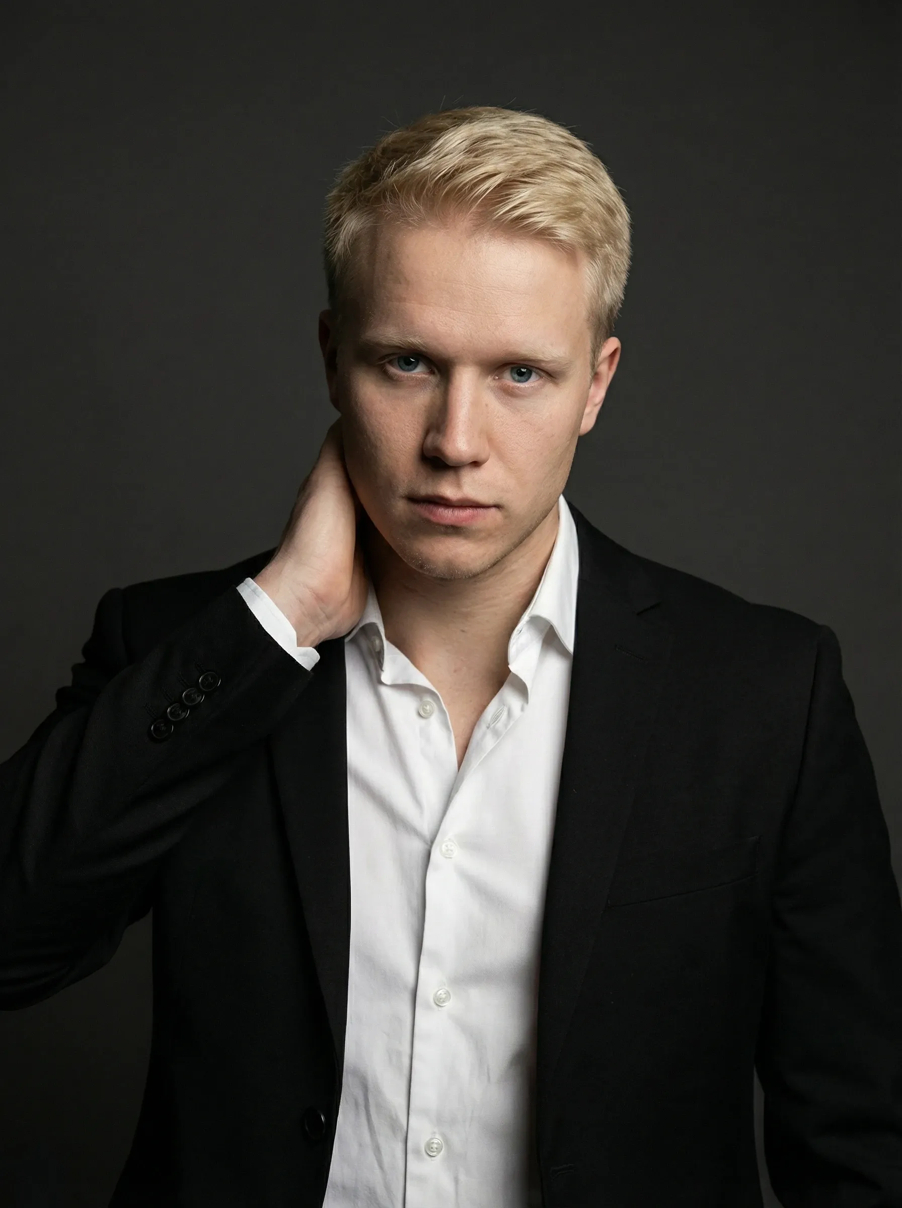 AI actor headshot — man in a black blazer and open white shirt against a dark studio background
